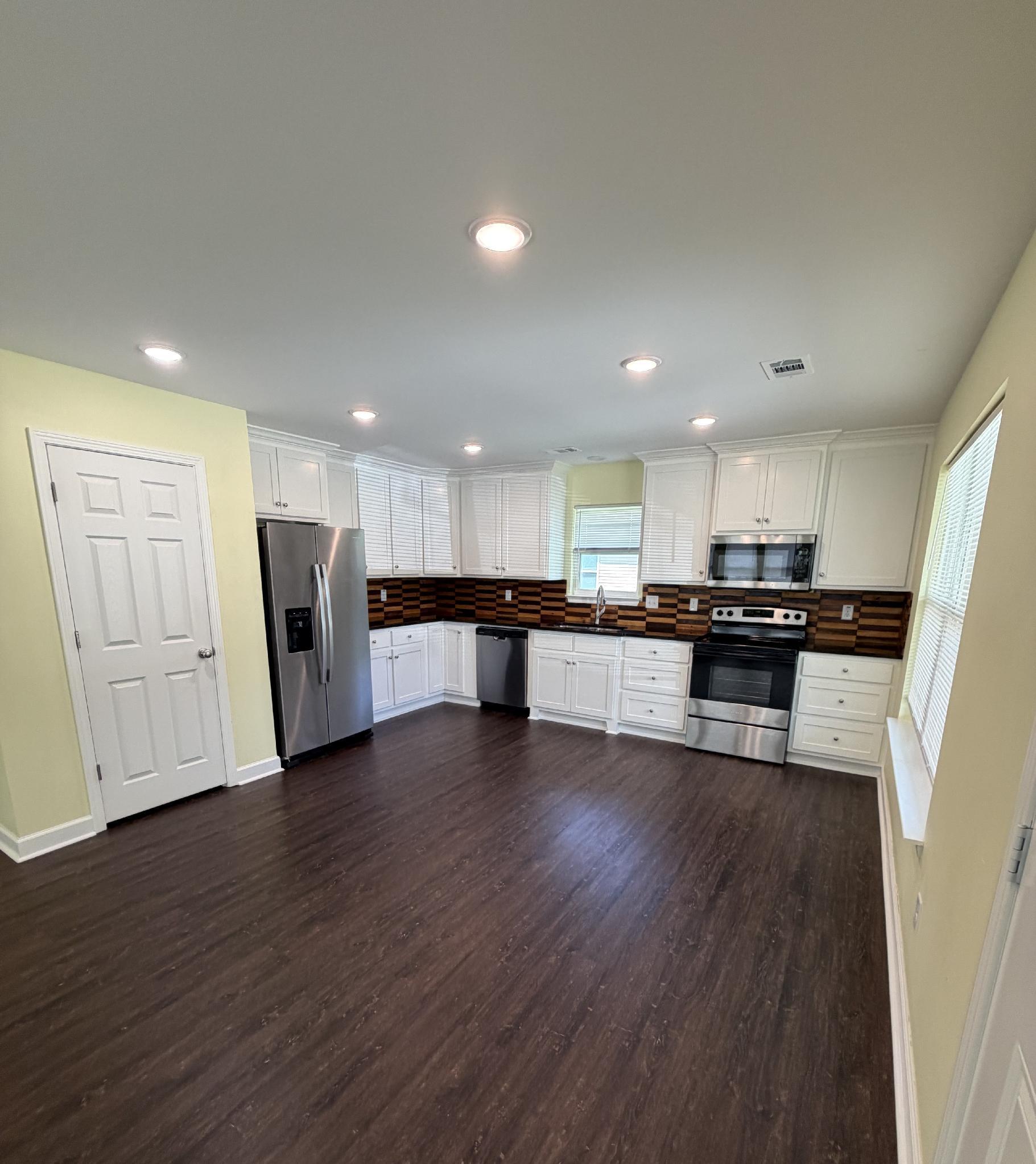 Open kitchen with white cabinets, wood backsplash and vinyl plank flooring